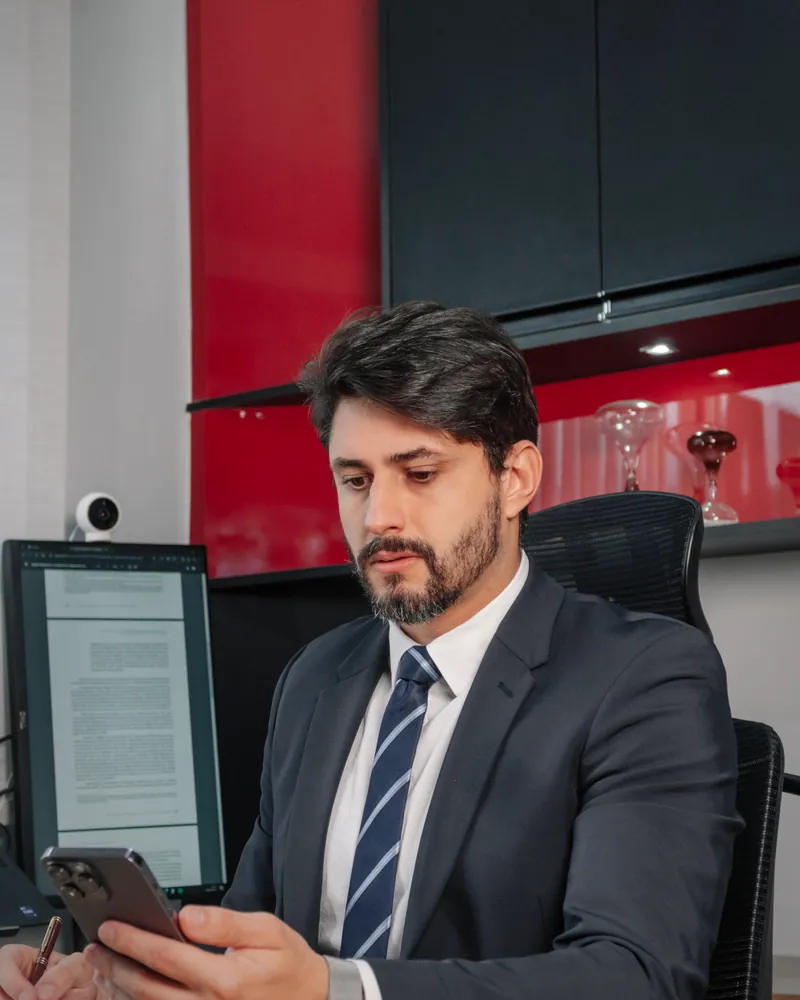 Dr. Washington lendo uma mensagem no celular, sentado à mesa do escritório